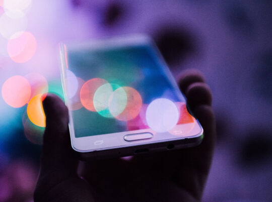 A person holding up a smartphone in their hand with colorful bokeh circles over its screen