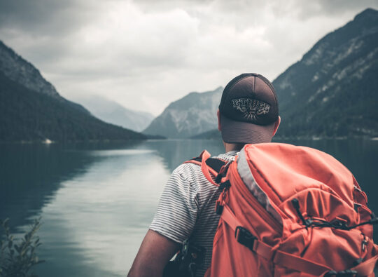Hiker with a heavy backpack looking out at mountains and still water